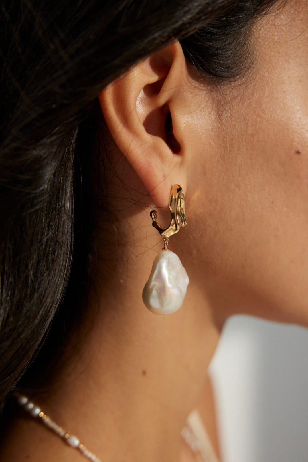 Close-up of a model wearing bold baroque pearl earrings with a fluid 18k gold design, styled for a beach wedding or vacation