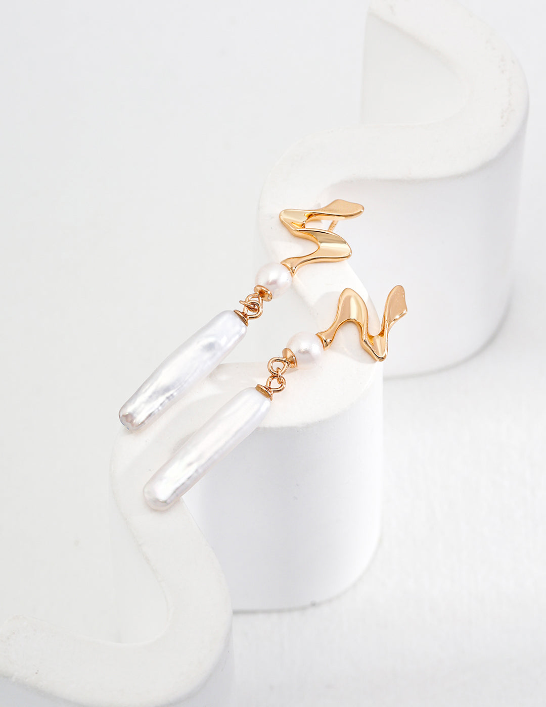 Minimalist abstract wave earrings in gold with baroque pearl pendants, photographed as a single-piece close-up