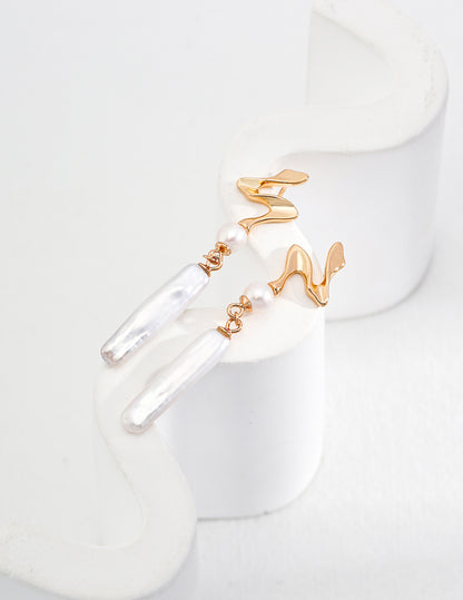 Minimalist abstract wave earrings in gold with baroque pearl pendants, photographed as a single-piece close-up