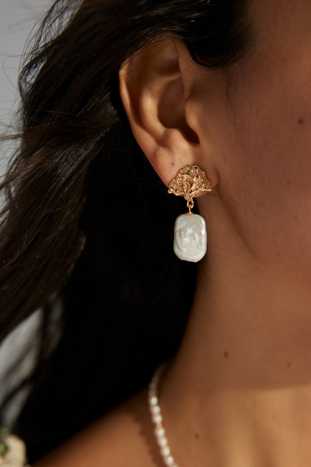 Gold leaf drop earrings with baroque pearl pendants, worn by a model in natural light for a timeless, sophisticated look